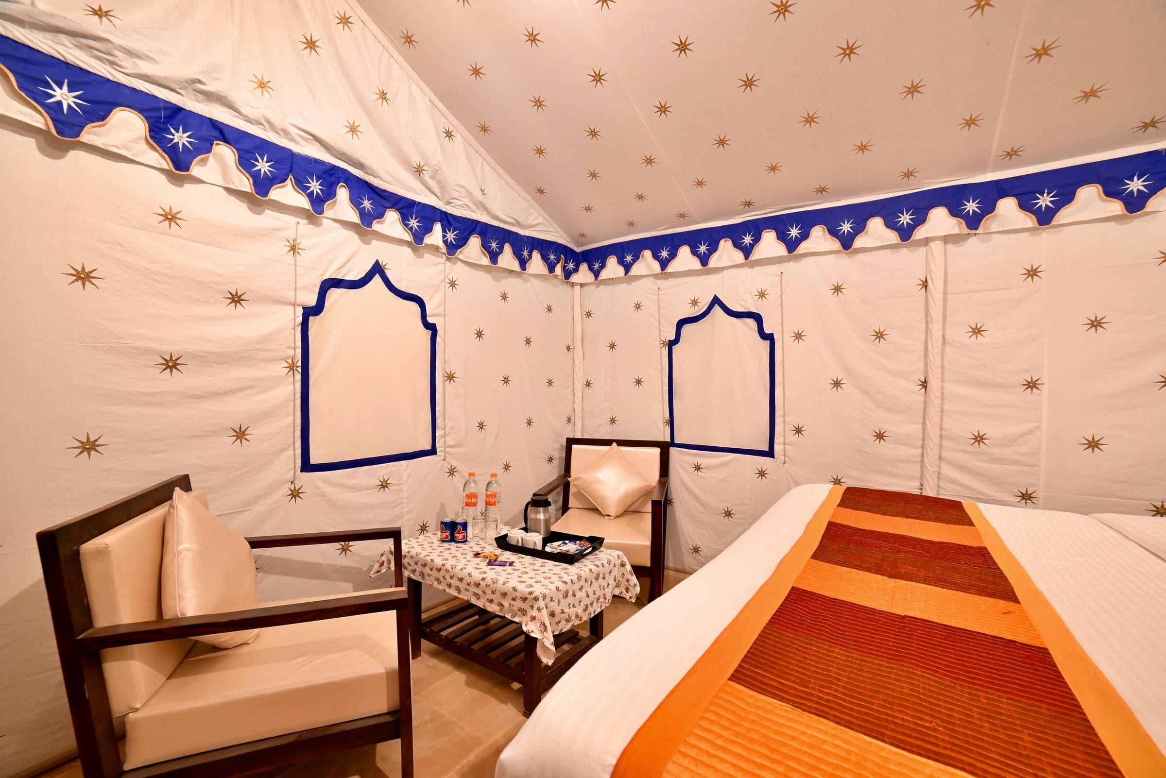 Inside a Royal Swiss Tent — star-embroidered canvas walls and ceiling, seating corner with tea tray, double bed with orange runner